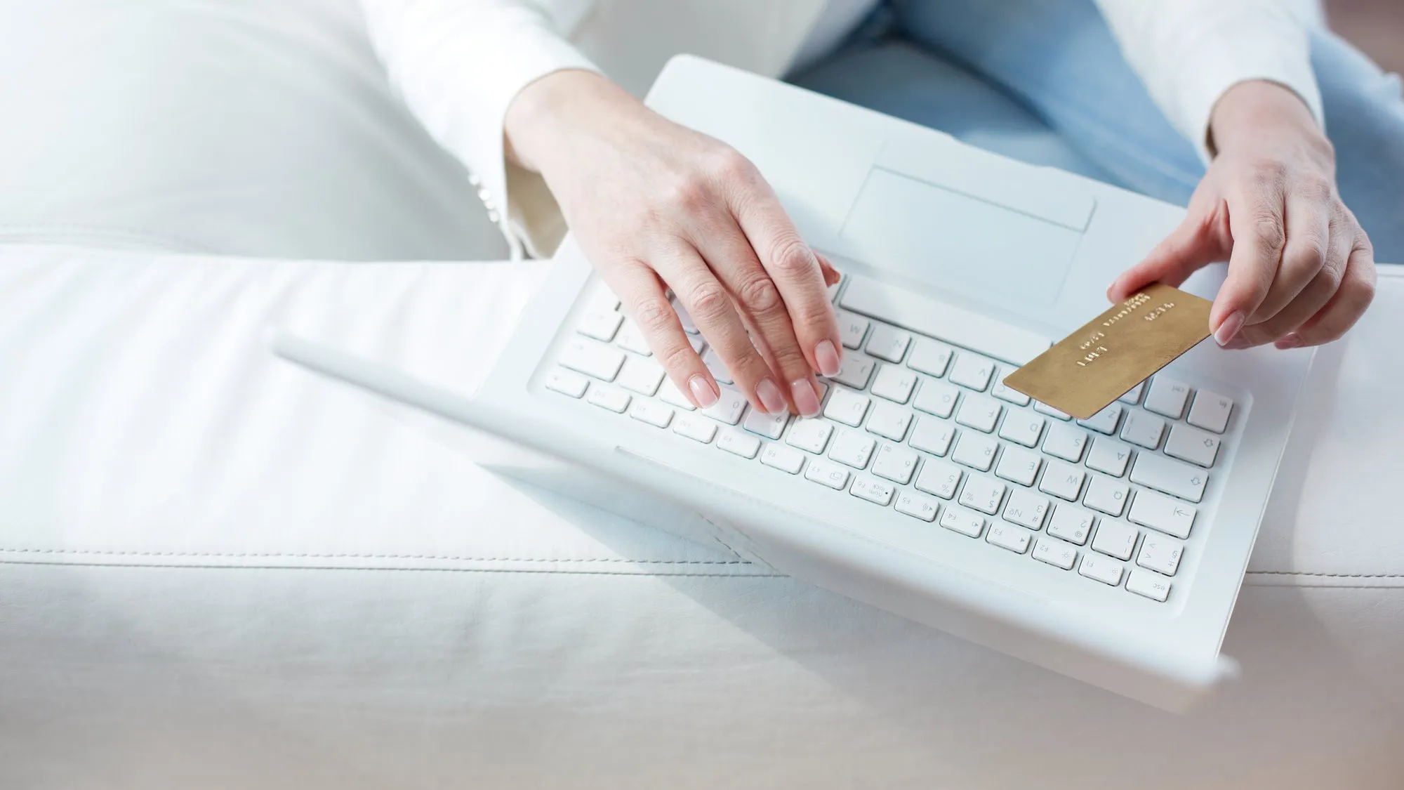 Close-up of a person's hands typing on a white laptop while holding a gold-colored payment card