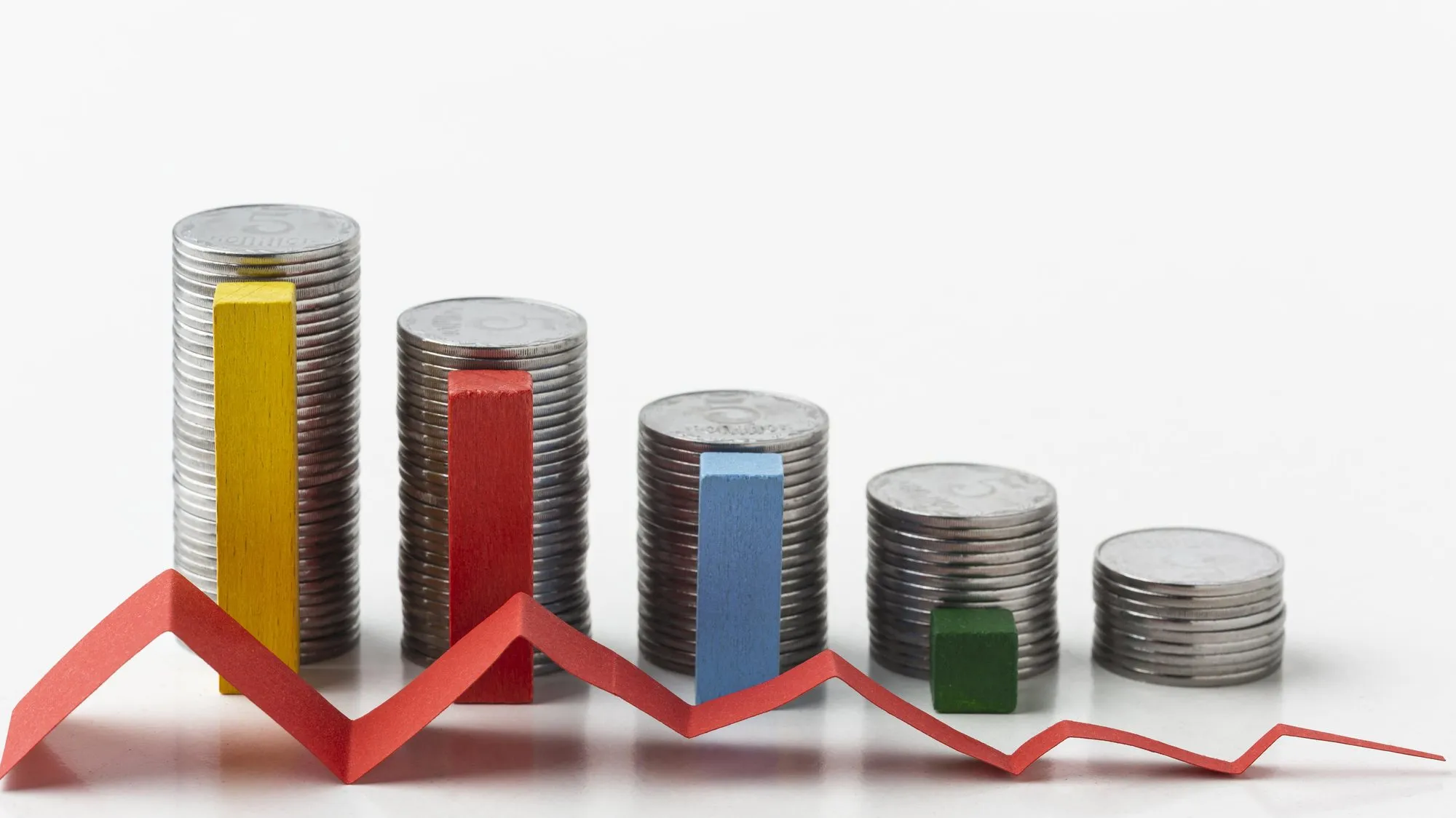 Stacks of coins getting shorter from left to right, with colored wooden blocks and a red paper line zigzagging downward in front of them