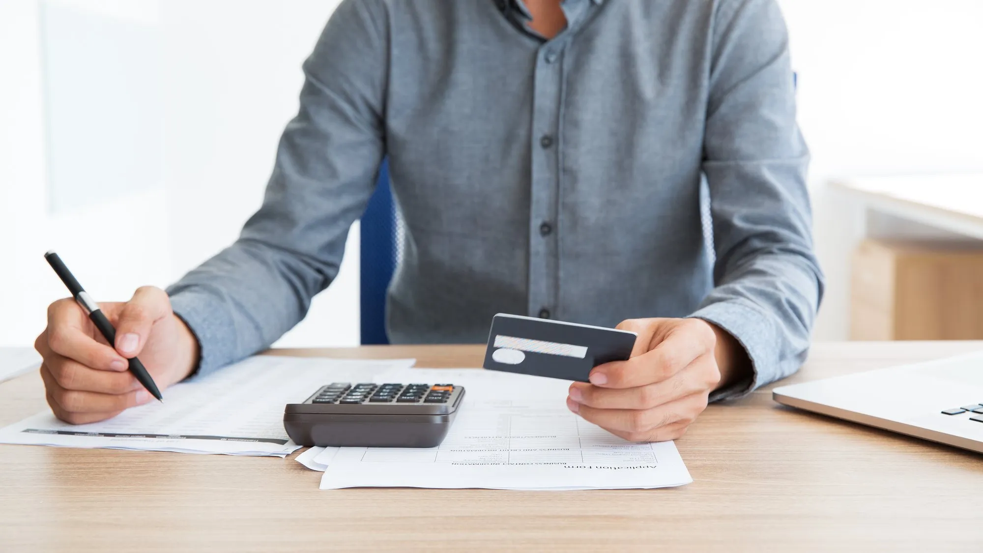 A person at a desk holding a credit card and a pen, with a calculator and loan paperwork in front of them